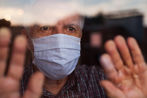 Elderly man wearing mask in nursing home looks out a window