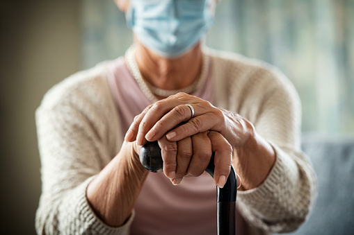 Close up of senior woman's hands holding walking stick and wearing face protective mask in nursing home during covid19 pandemic. 